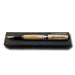 An Americana Pens and Pencils writing instrument with a wooden barrel, engraved and accented in gold and silver, sits elegantly on a black rectangular stand.